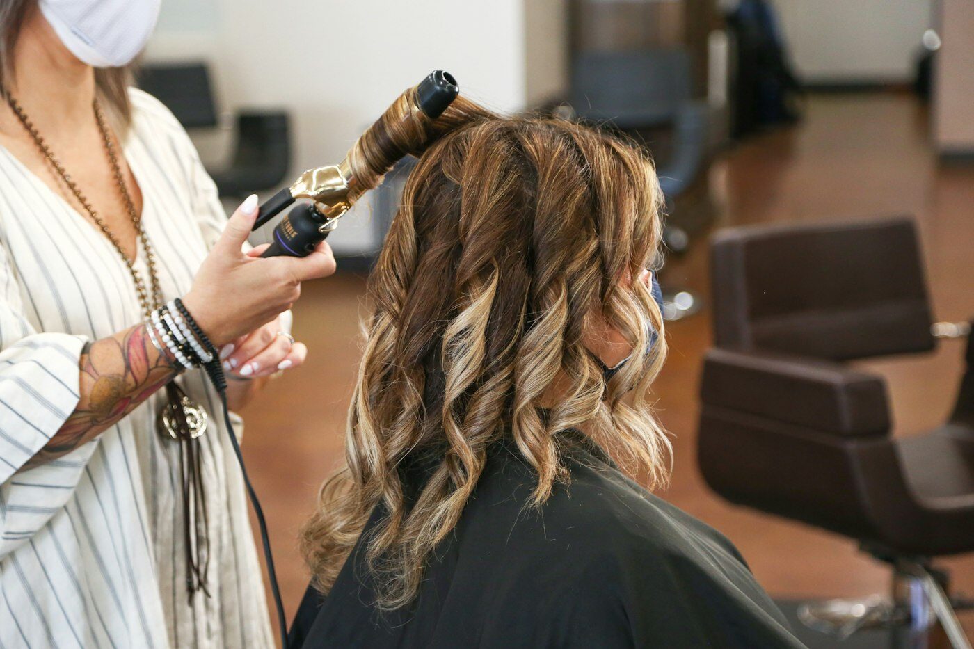 Stylist shaping soft waves in a client's long brunette hair with a curling iron