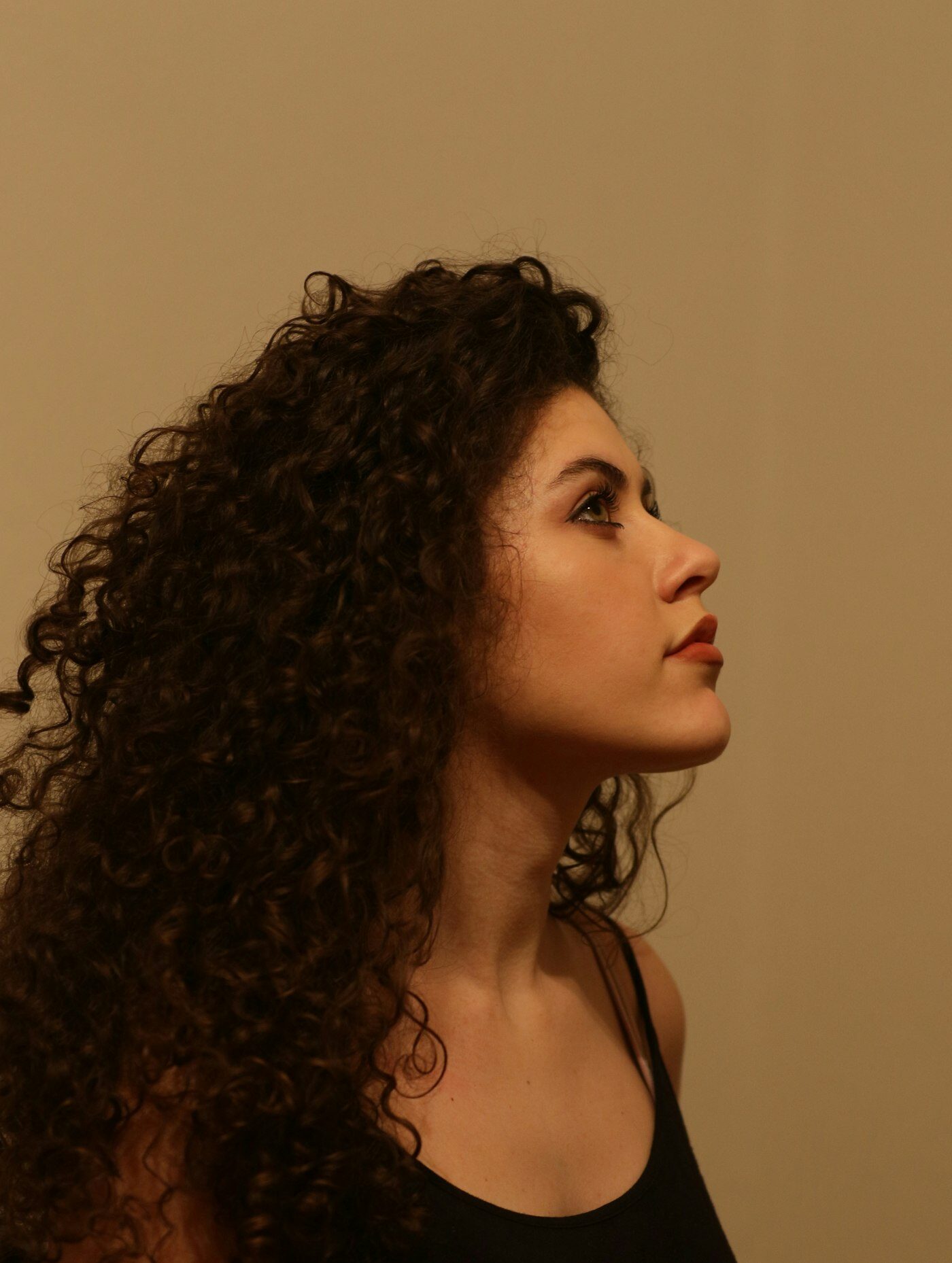Side profile of a woman with long, defined curls against a warm backdrop