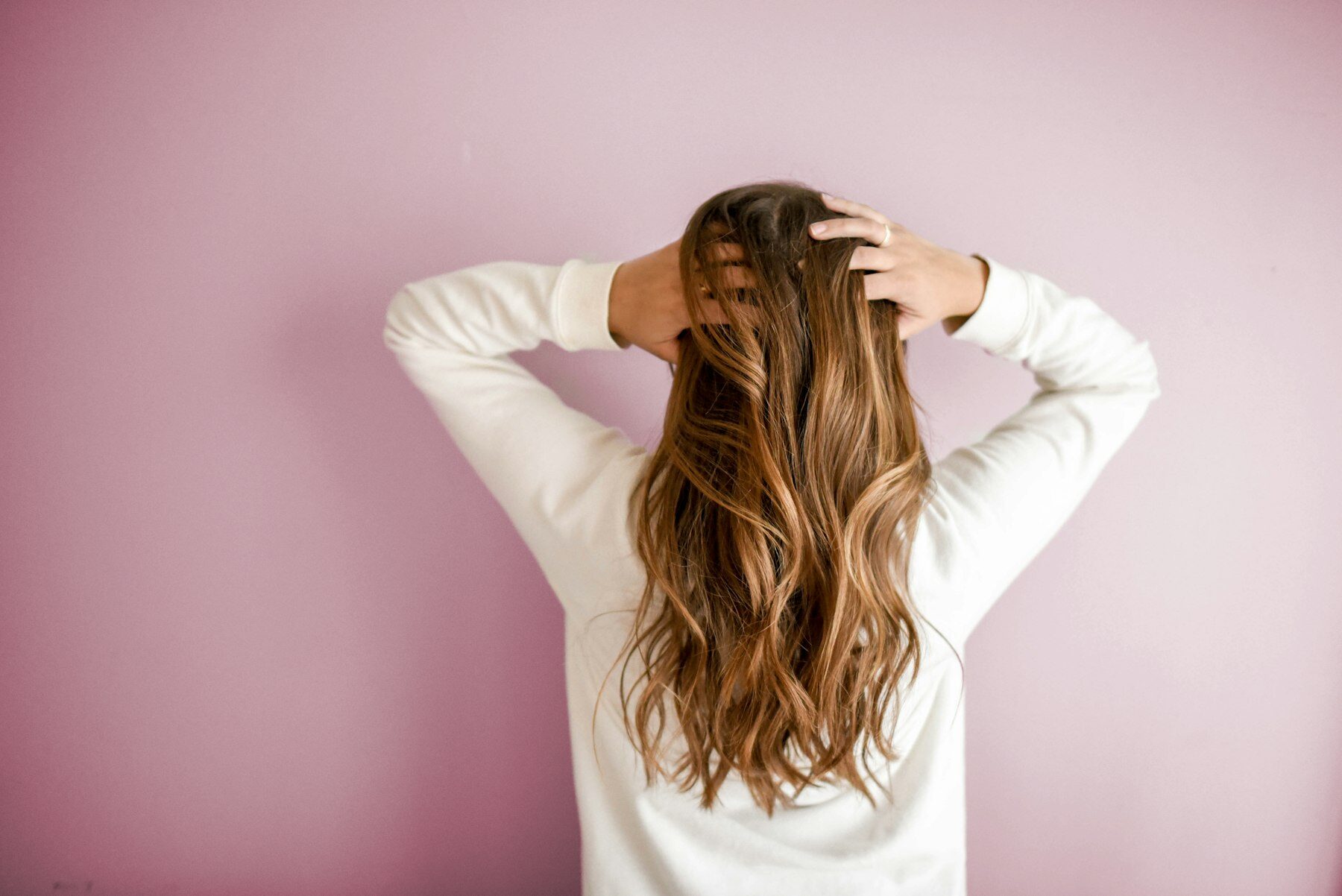 Woman seen from behind running a hand through long, softly waved caramel hair