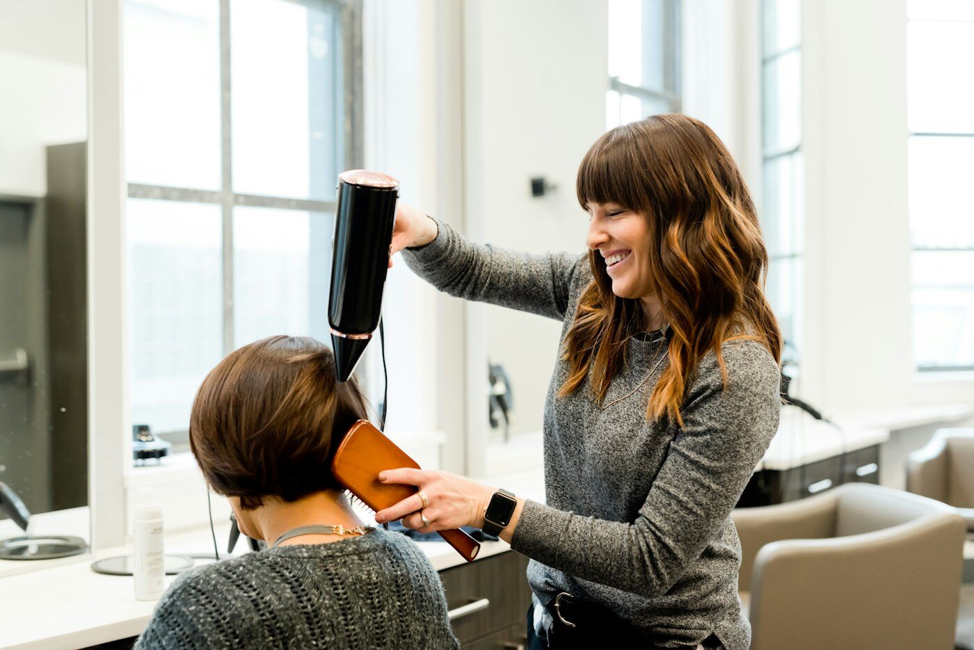 Stylist blow-drying a client's hair in a bright salon